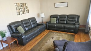 A living room with two black leather sofas, a wooden coffee table, a small side table with a plant, a floor lamp, and a rug.