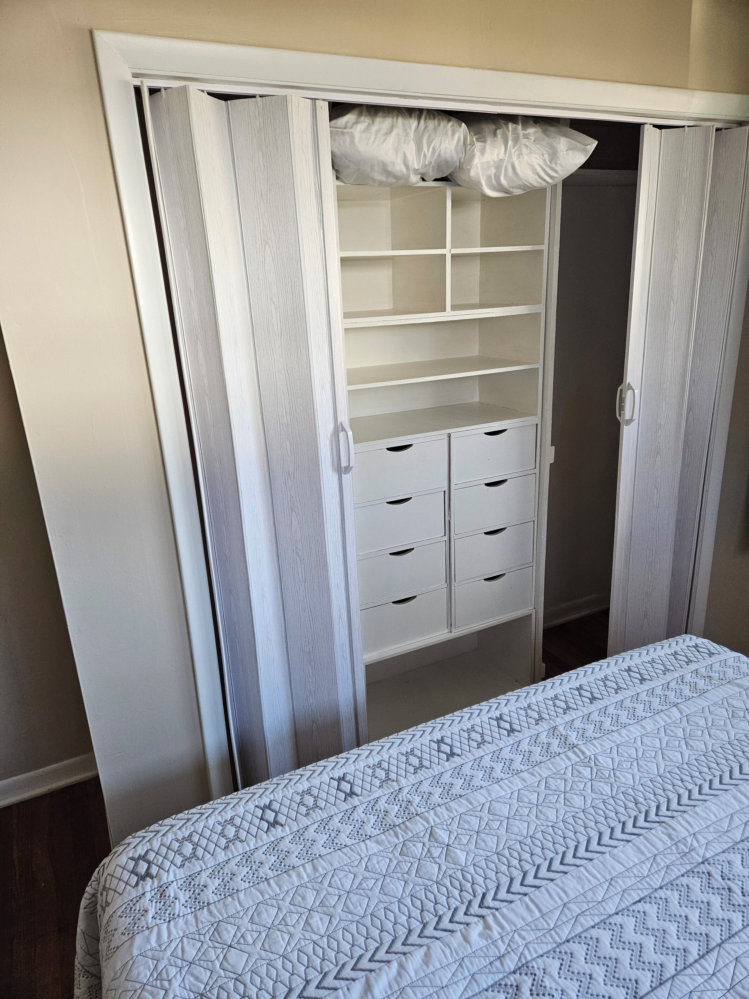 Ein Schlafzimmer mit einem Bett, einem weißen Kleiderschrank mit Schubladen und einem Wandregal.