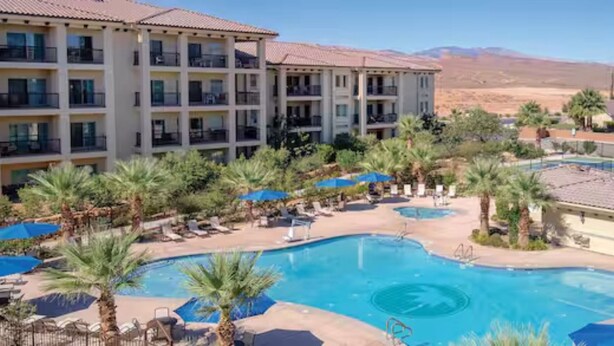 Un hotel amb una piscina gran, palmeres i un paisatge desertic al fons.