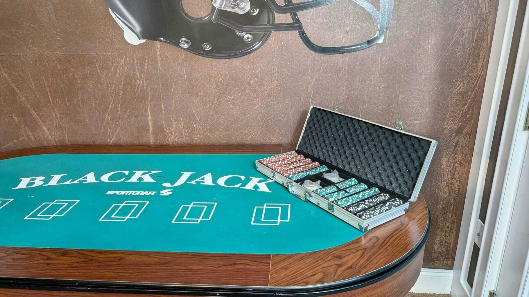 A blackjack table with a 'BLACK JACK SPORTCRAFT' sign, a set of dice, and a card deck in a case.