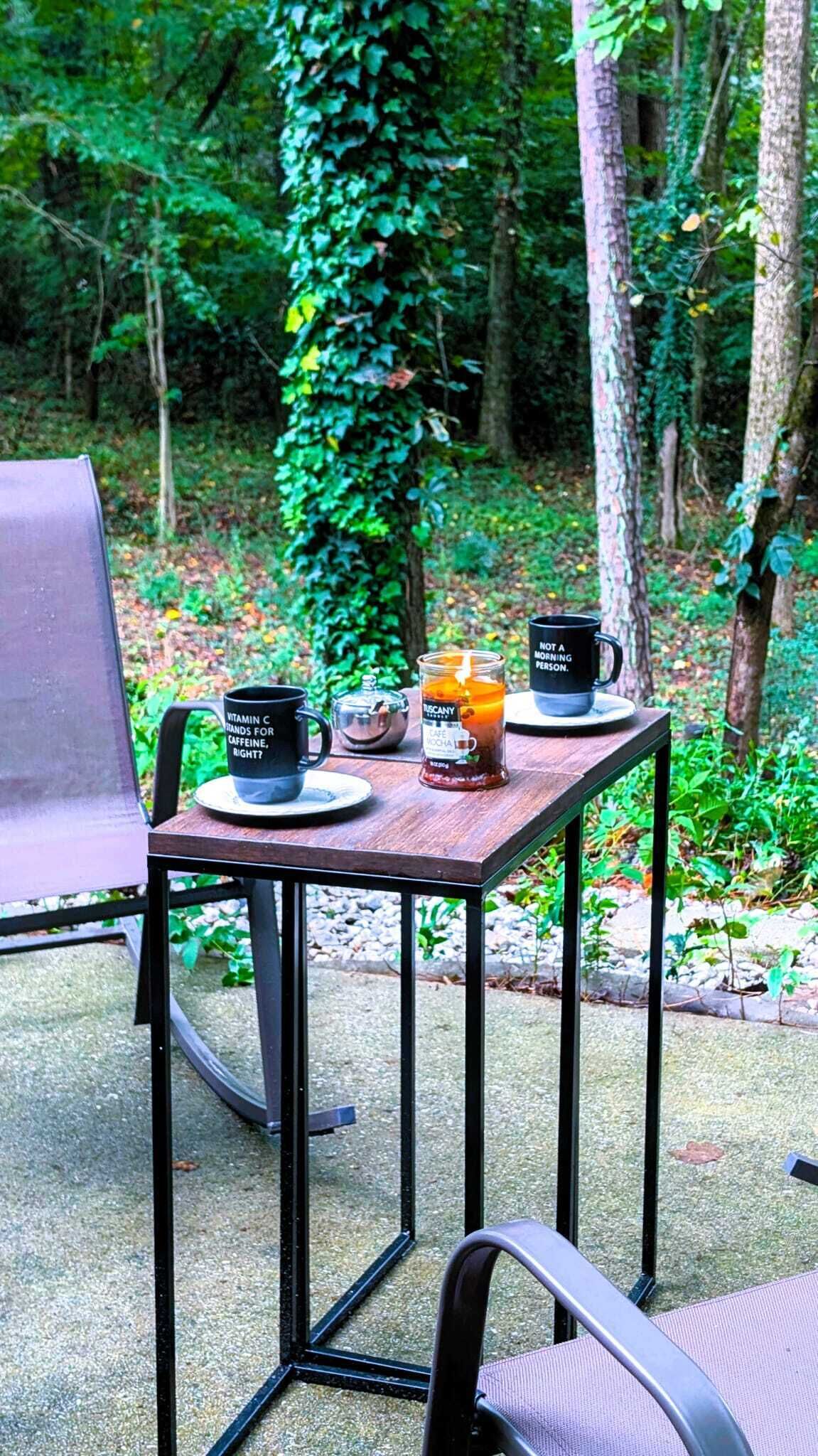 A table with two black mugs, one labeled "Vitamin C" and the other "Not a morning person," and a glass jar with a tea infuser.