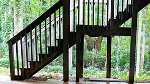 A wooden staircase with a metal railing leading to a platform surrounded by lush greenery. - Cozy 2BR Retreat • Near Lake Lanier & Mall of GA • Private, Peaceful, Festive


 (Sugar Hill)