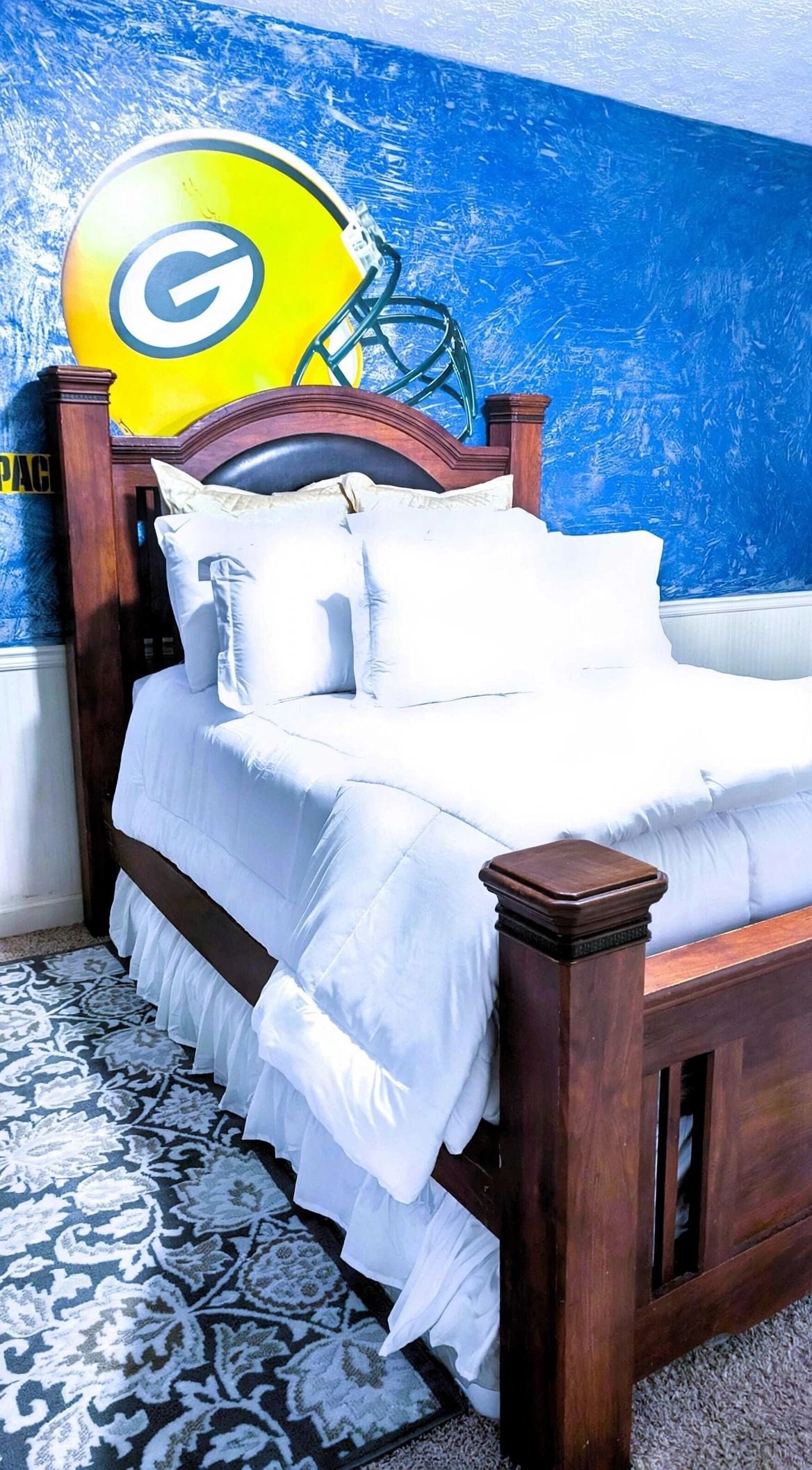 A bed with white bedding, a wooden headboard, and a patterned rug on a carpeted floor.