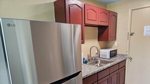 Cocina compacta con refrigerador de acero inoxidable, microondas y armarios de madera.
