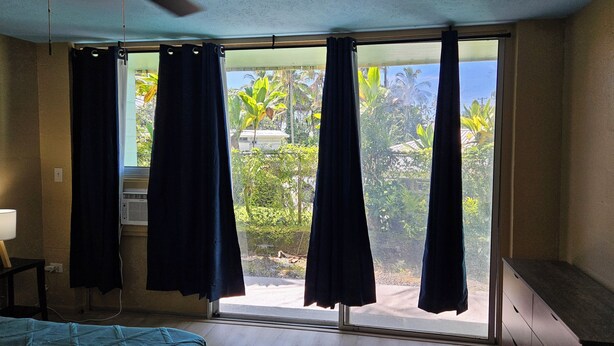 Una habitación con cama, ventilador de techo y ventana con cortinas.