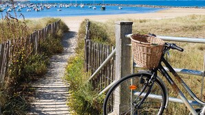 A bicycle with a basket parked on a wooden path leading to a beach with boats. - Beautiful apartment with WiFi (Pornic)