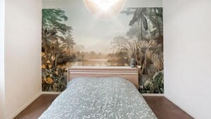 A bedroom with a bed, a wall mural of a tropical landscape, and a hanging light fixture. - Beautiful apartment with WiFi (Pornic)