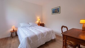 A bedroom with a bed, two bedside tables with lamps, a wooden chair, a wooden table, and a framed picture on the wall.