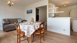 A dining area with a table set for four, a sofa, and a kitchen area with a white countertop and cabinets.