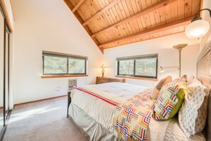 A bedroom with a wooden ceiling, two windows, a bed with a colorful blanket, and a bedside lamp. - Dwell at Tahoe Donner by Tahoe Getaways - 3BR w Private Sauna + HOA Amenities! (Truckee)