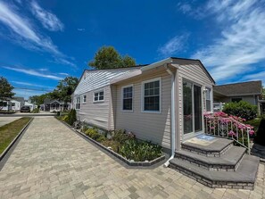 A single-story mobile home with a front porch, a paved driveway, and a small garden area.