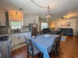 A modern kitchen with white cabinets, a dining table with a patterned tablecloth, and a black leather couch in the living area.