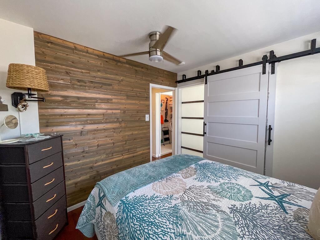 Un dormitorio con cama, cómoda, armario, ventilador de techo y pared de madera.