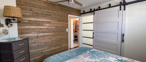 Un dormitorio con cama, cómoda, armario, ventilador de techo y pared de madera.
