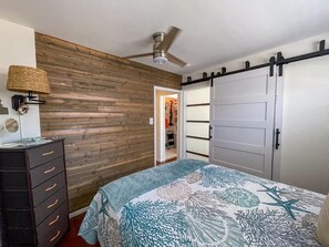A bedroom with a bed, dresser, wardrobe, ceiling fan, and a wooden wall.