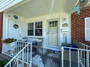 A porch with wicker furniture, a white door, and a brick wall.