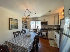 A kitchen with a dining table, chairs, a chandelier, cabinets, a refrigerator, and a stove.