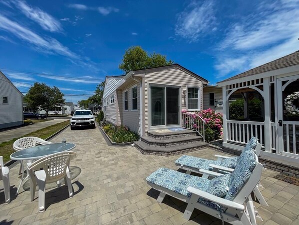 A patio area with lounge chairs and a table, a covered seating area, and a small house with a porch.