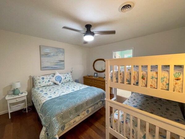 A bedroom with a bed, a nightstand, a dresser, a crib, a ceiling fan, and a window.