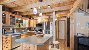 A spacious kitchen with wooden cabinets, a central island with stools, stainless steel appliances, and pendant lighting. - Charming Cabin in Seven Devils (Seven Devils)