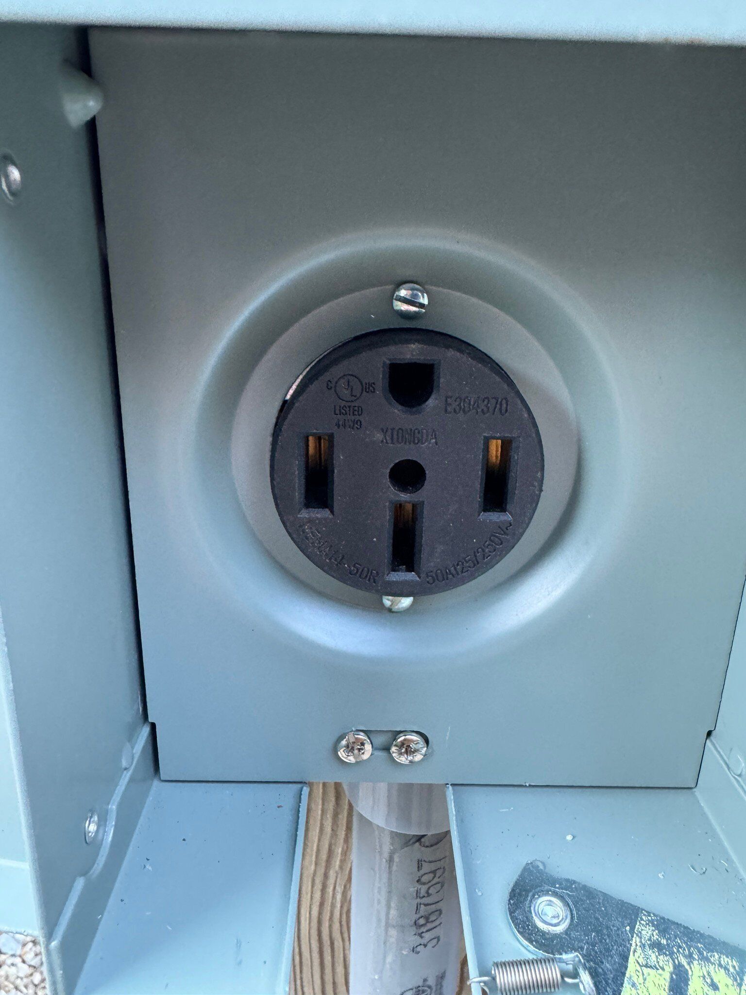A gray electrical box with a circular outlet, visible screws, and a metal plate with text.