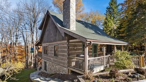 A log cabin with a stone chimney, a porch with a railing, and a stone foundation. - Charming Cabin in Seven Devils (Seven Devils)