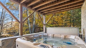 A hot tub with a stone exterior, set under a wooden pergola with a view of autumn trees. - Charming Cabin in Seven Devils (Seven Devils)