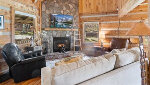A cozy log cabin interior with a stone fireplace, leather seating, and a television mounted on the wall. - Charming Cabin in Seven Devils (Seven Devils)