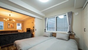Ein Schlafzimmer mit zwei Betten, einem hölzernen Kopfteil, einem Fenster mit Vorhängen, einer Deckenleuchte und einer eingebauten Bank mit Kissen.