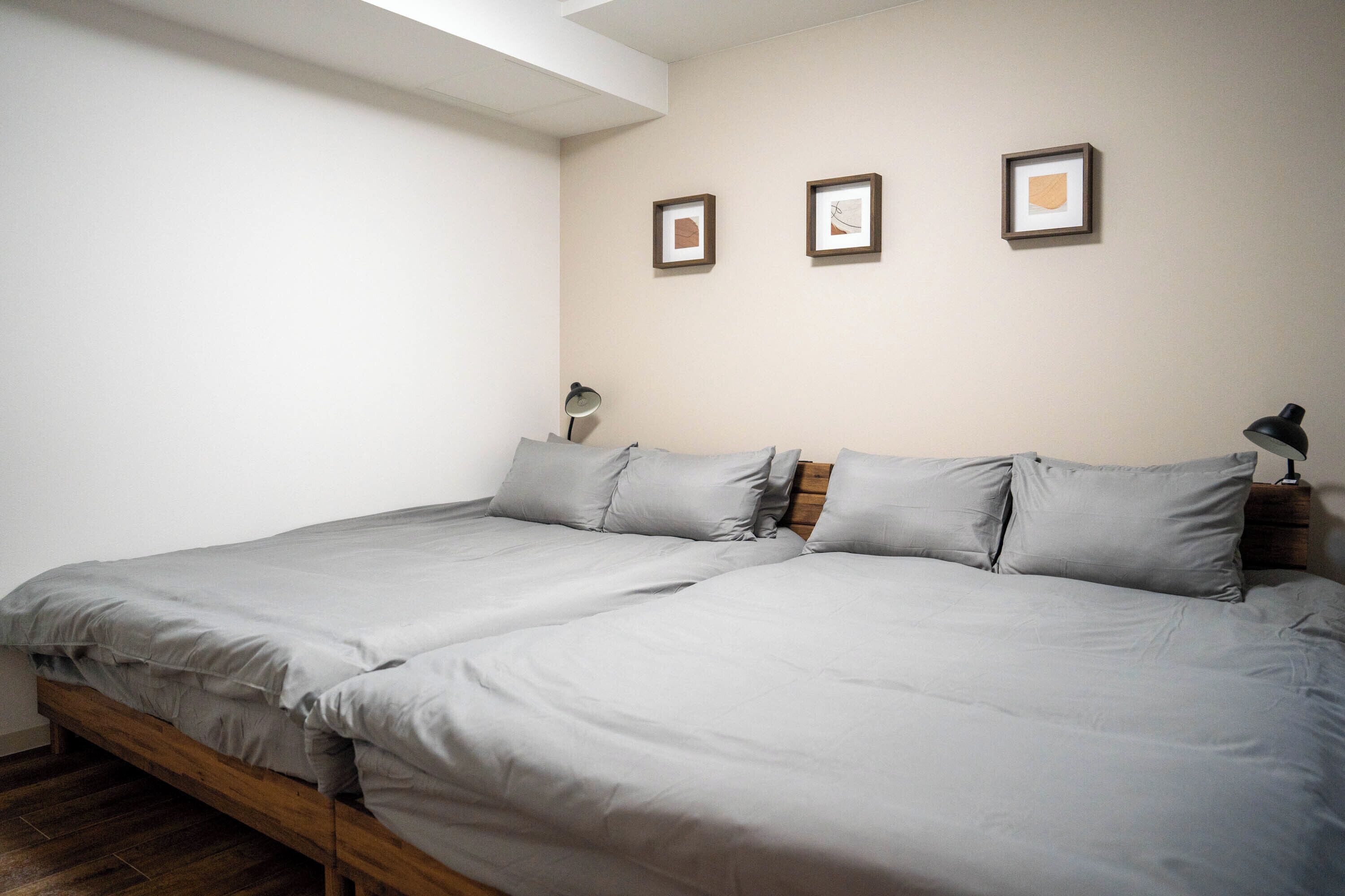 A bedroom with two beds, a wooden floor, and three framed pictures on the wall.