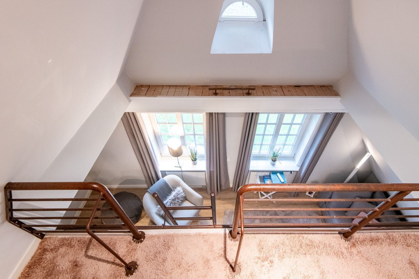 A loft bedroom with a sloped ceiling, a skylight, a view of the outdoors, a wooden floor, and a small window.