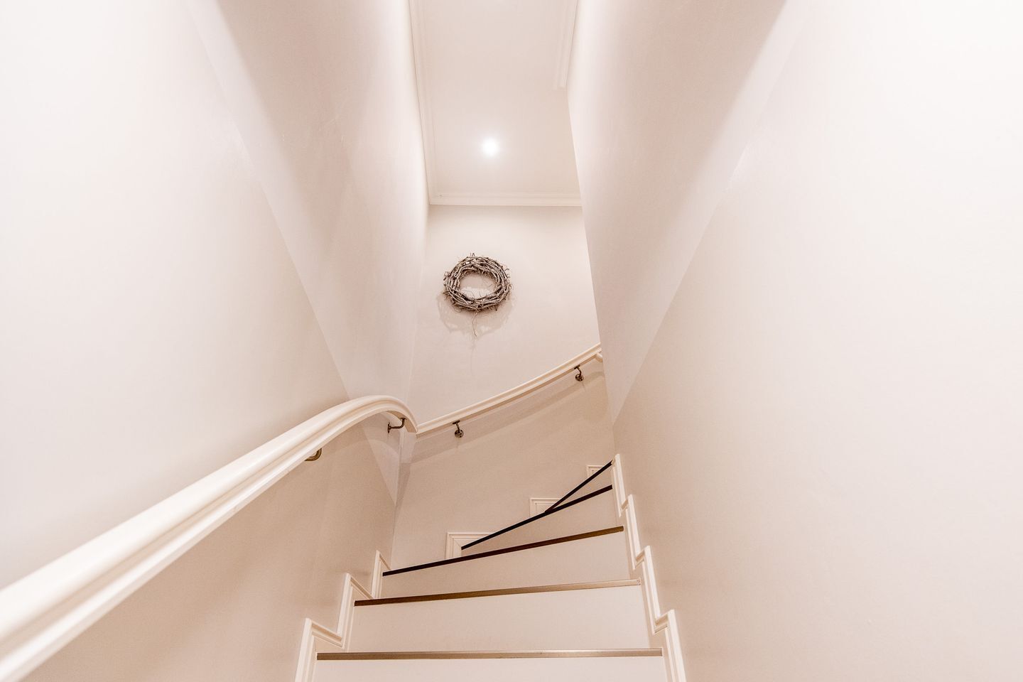 Eine Treppe mit weißen Wänden und schlichtem Design, die zu einer Zwischenebene mit einem Kranz an der Wand führt.