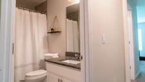 Un baño con inodoro blanco, lavabo con encimera de granito, espejo y cortina de ducha.