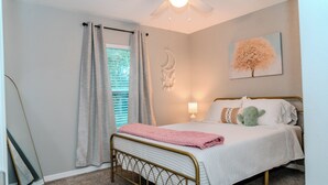 Un dormitorio con cama, ventilador de techo, ventana con cortinas, lámpara de pared y decoración de cactus.