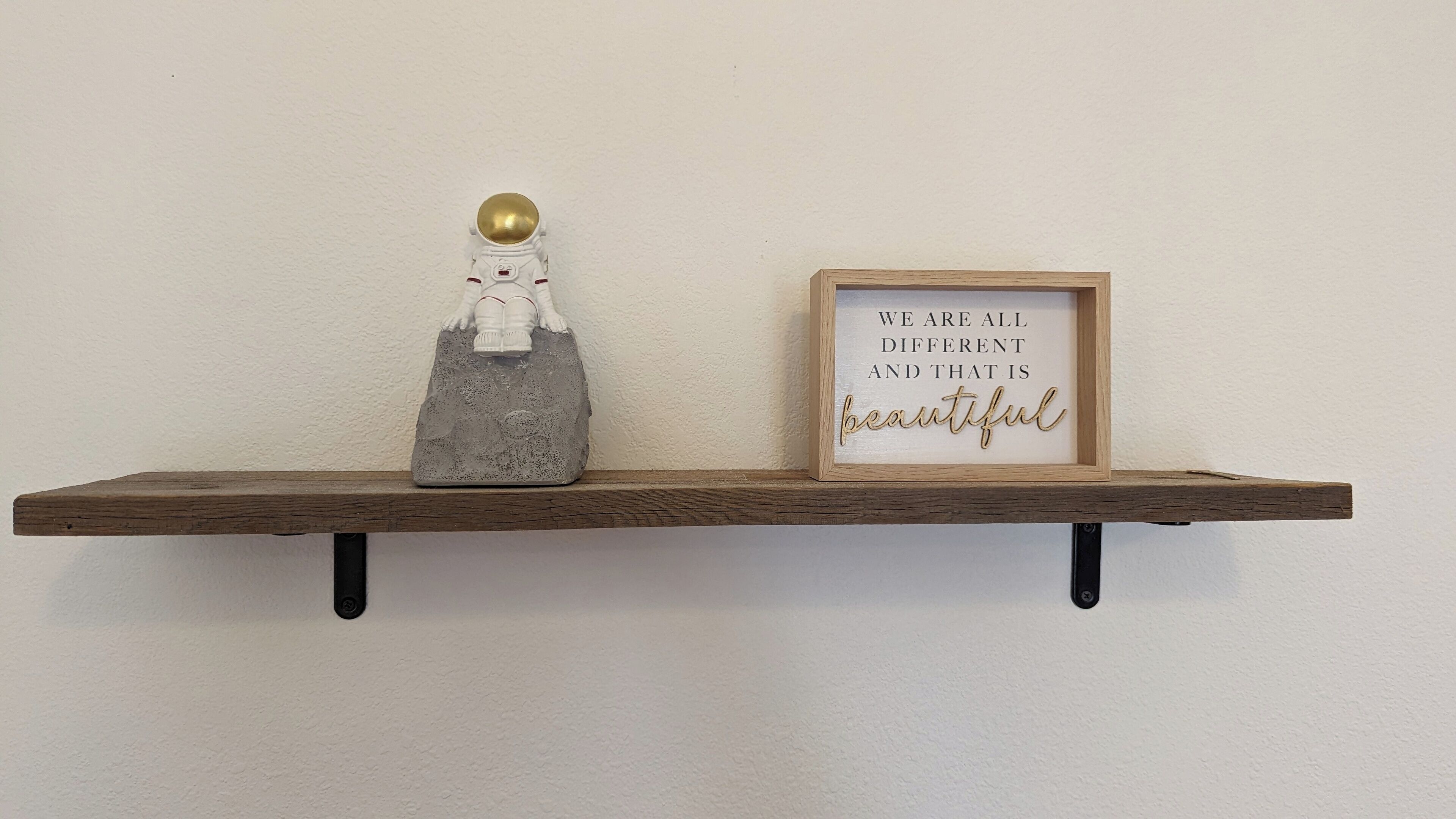 A wooden shelf with a figurine and a framed inspirational quote.