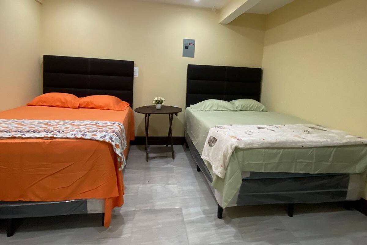 A room with two beds, a small table, and a ceiling light.