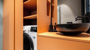 Une cuisine moderne dotée d’un lave-linge encastré, d’un saladier noir posé sur le plan de travail et d’armoires en bois.
