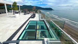 Terraço no telhado com piscina infinita de vidro, área de estar ao ar livre e vista para a praia e oceano.