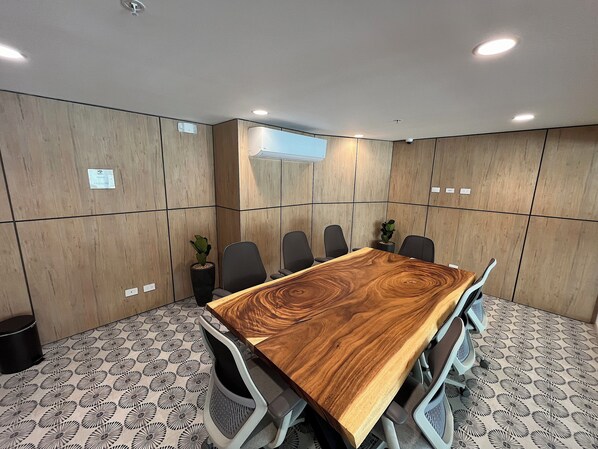 A conference room with a wooden table, six chairs, and a potted plant.