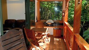 Een houten terras met een barbecue, stoelen en uitzicht op de omgeving.
