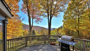 A wooden deck with a grill and a view of autumn trees.