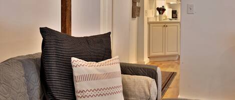 A living room with a grey couch, two pillows, and a view into the kitchen area.