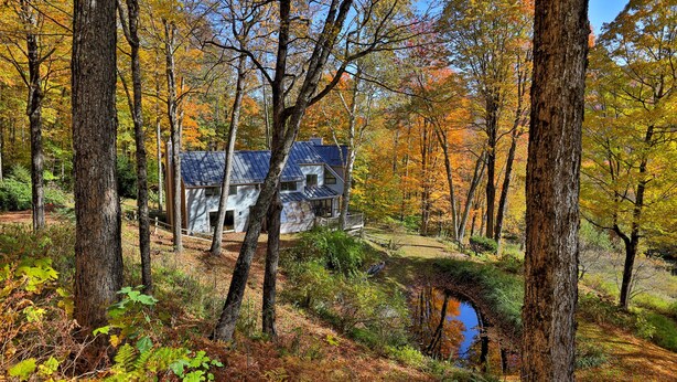 A rustic cabin surrounded by autumn foliage, with a small stream nearby.