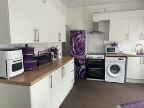 Een kleine keuken met witte kastjes, een magnetron, een fornuis en een wasmachine.