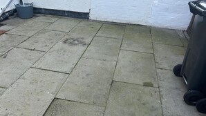Eine Beton-Terrasse mit einem grauen Eimer und einer schwarzen Mülltonne.