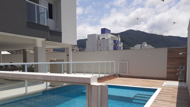 A rooftop pool with clear blue water, surrounded by a wooden deck and a white railing.