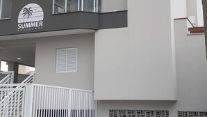 A multi-story building with balconies, a logo with palm trees, and a gated entrance.