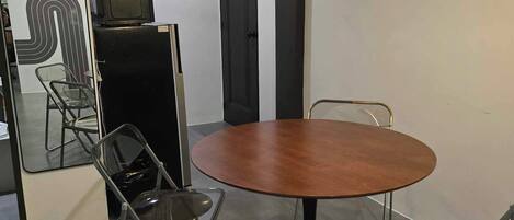 A modern dining area with a round table, metal chairs, a hanging light fixture, and a refrigerator.