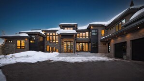 A modern multi-story house with a snow-covered roof and a well-lit entrance. - 6 Bedroom Ski In/Ski Out Luxury 6 Bedroom Private Gated Community (Park City)