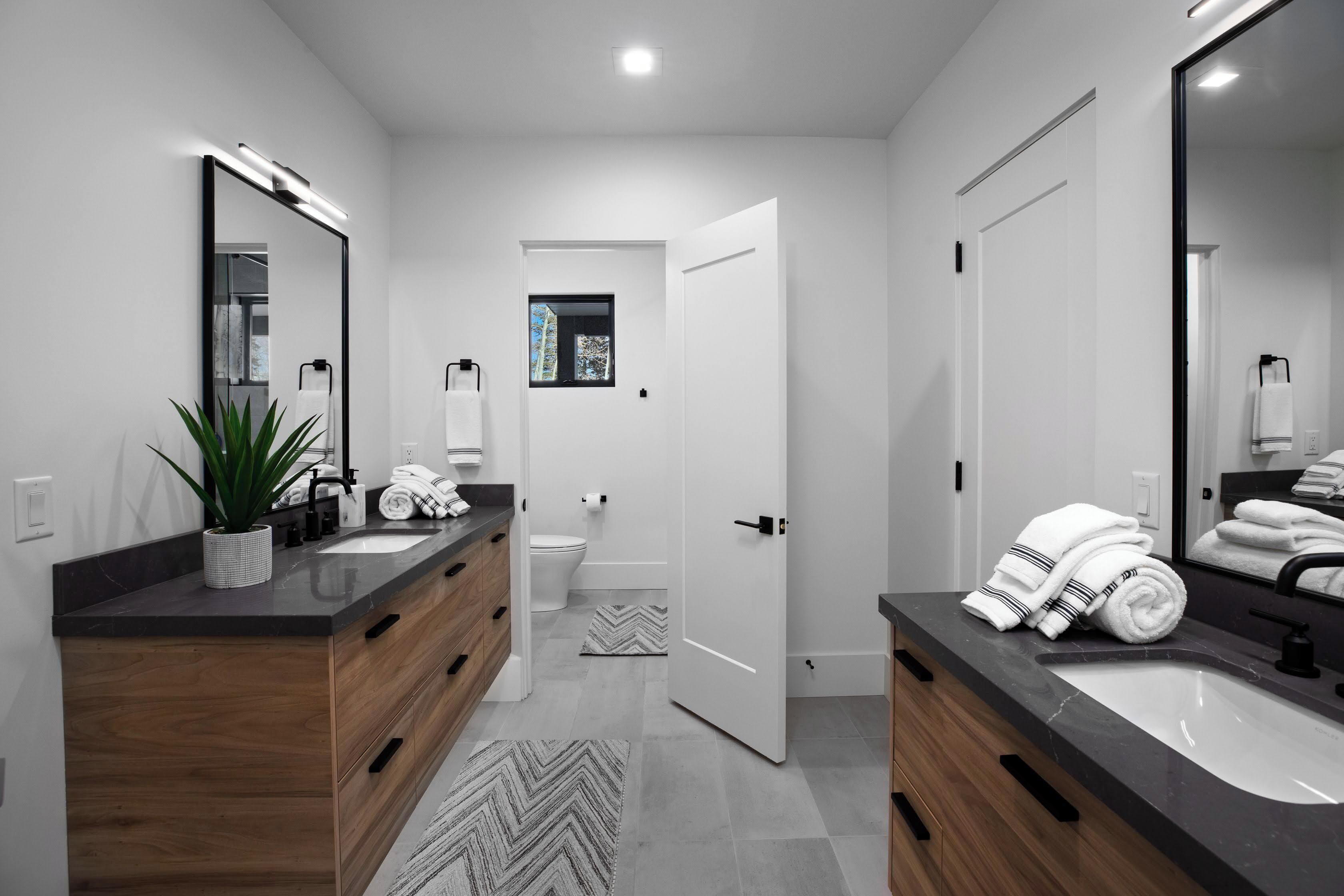 Un baño moderno con dos lavabos, armarios de madera, un espejo grande y una planta en maceta.